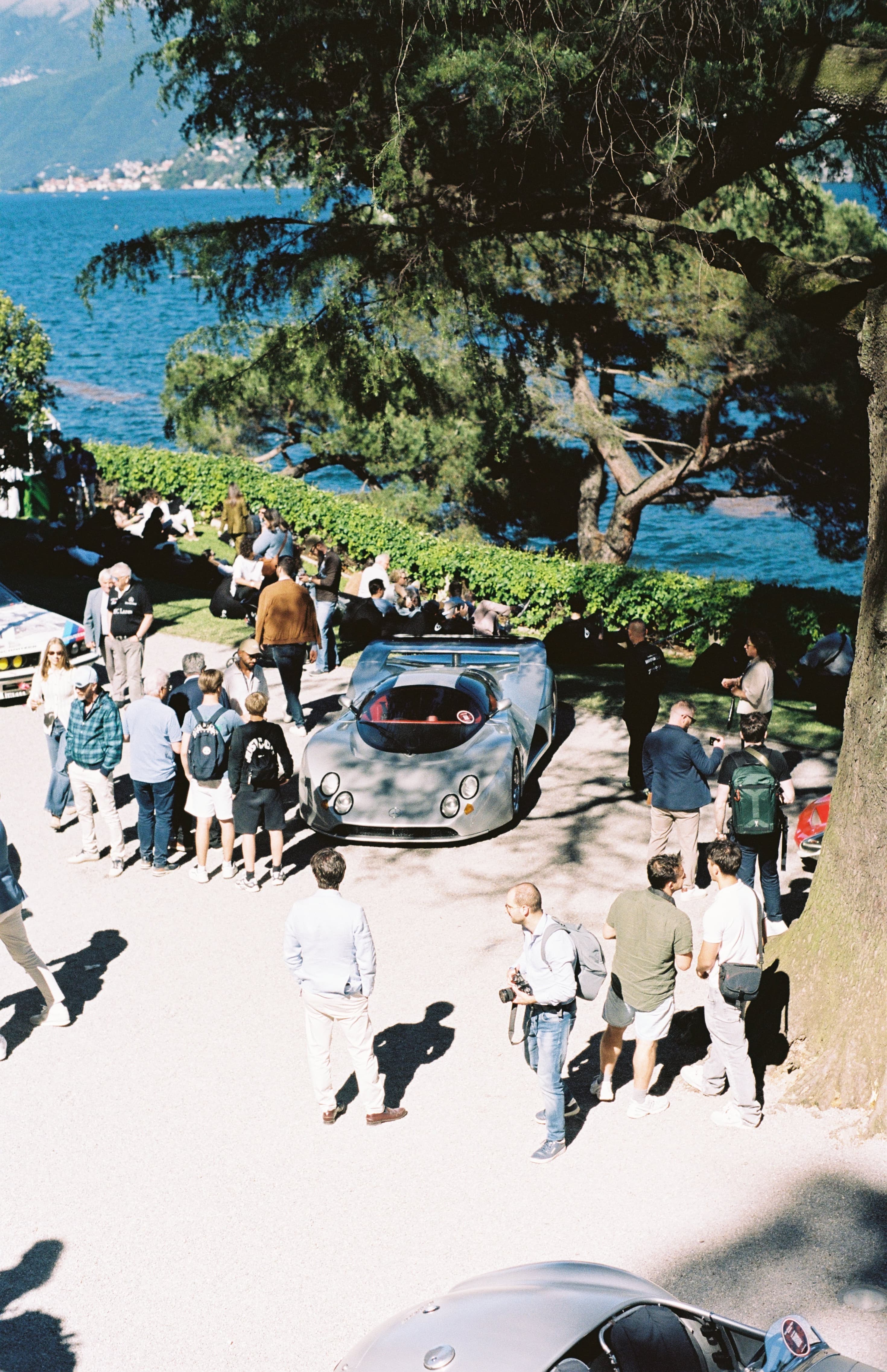 Car club event beside the water with attendees gathered around cars