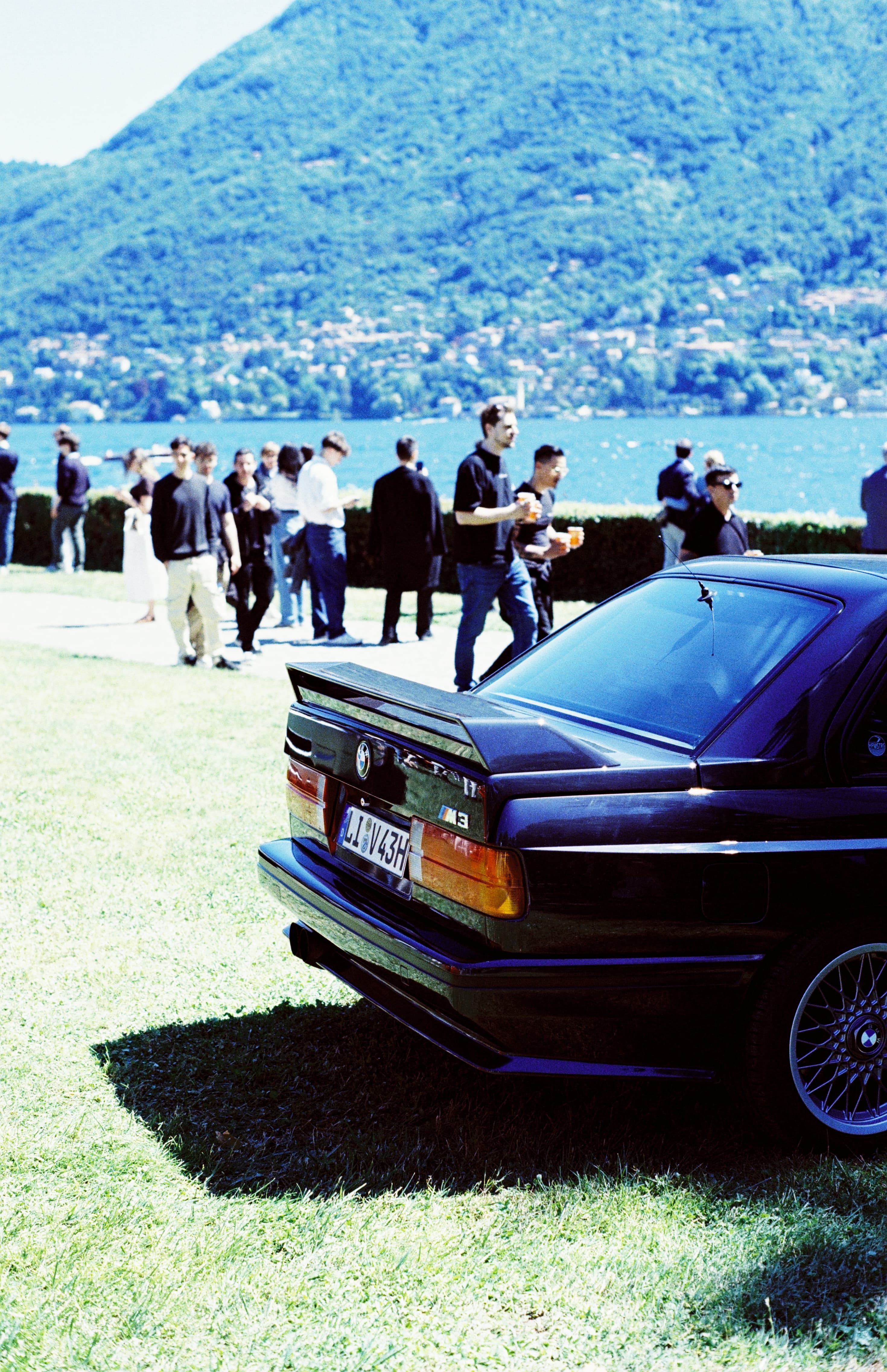 BMW M3 at a lakeside automotive event with guests in the background
